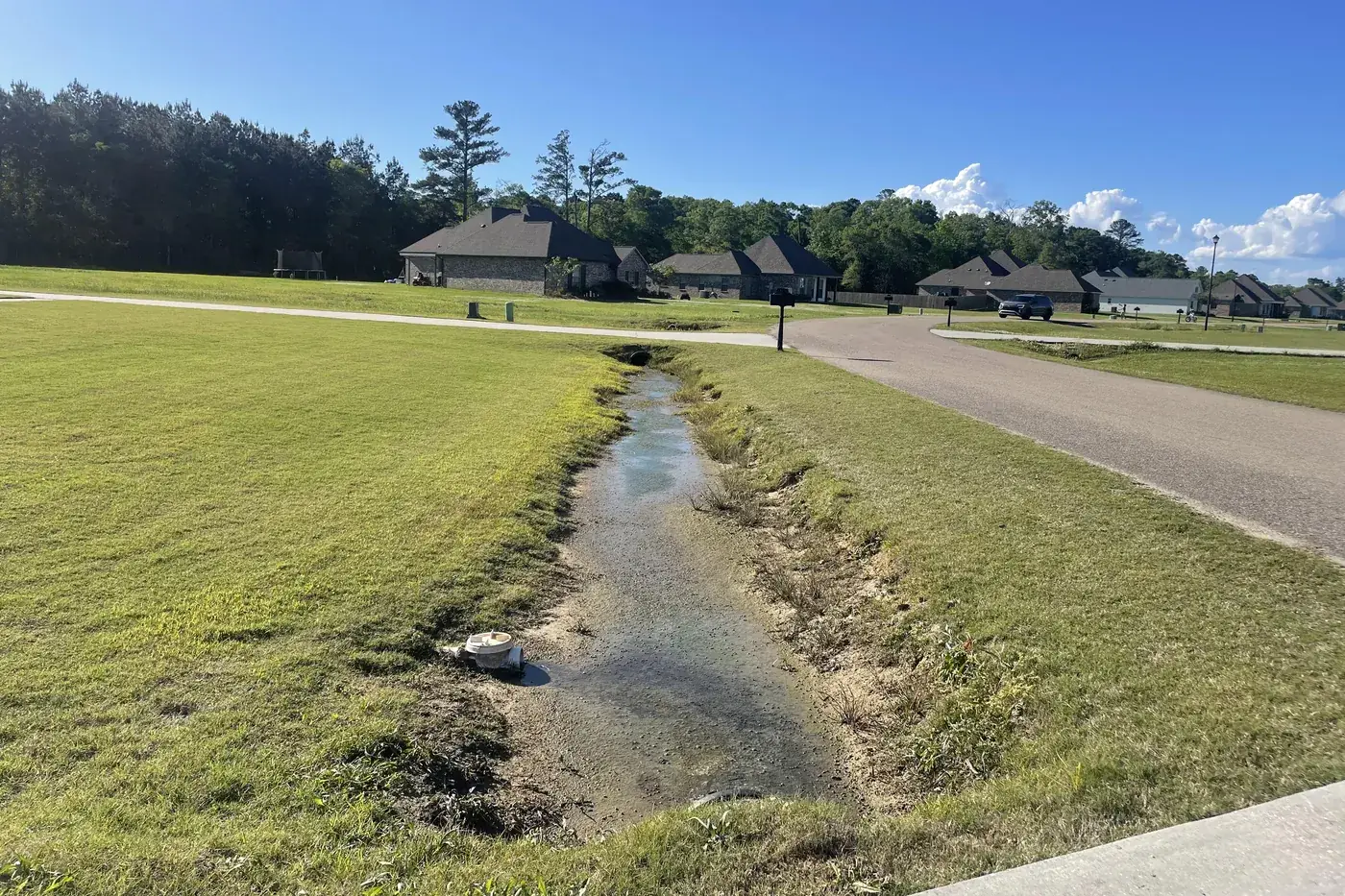 Grassy roadside ditch running to a driveway culvert beside a paved road