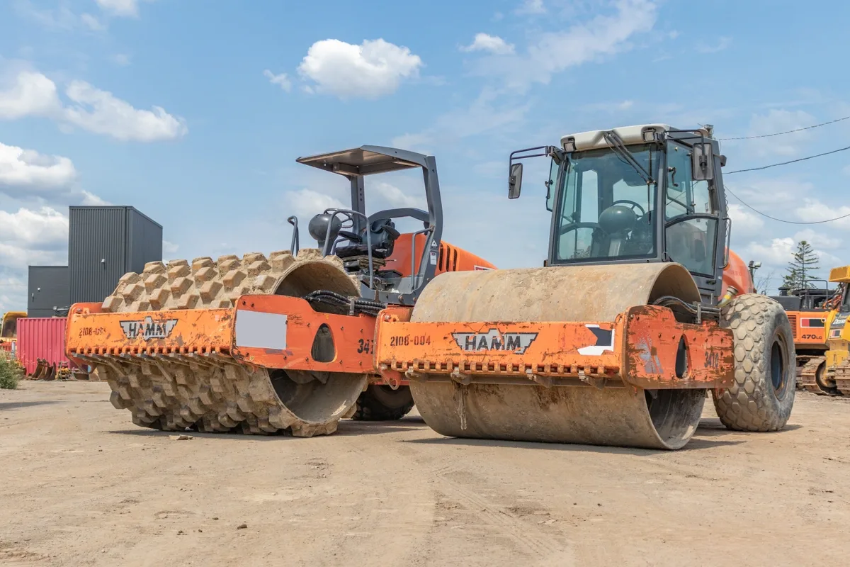 Two compaction rollers, one padfoot and one smooth drum, parked on a gravel lot